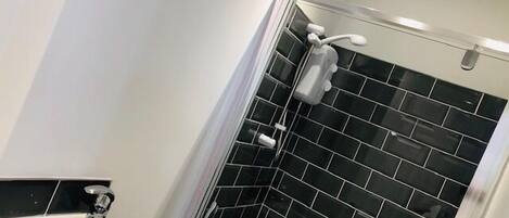 A bathroom with a white sink, black tiled shower walls, and a glass shower enclosure.