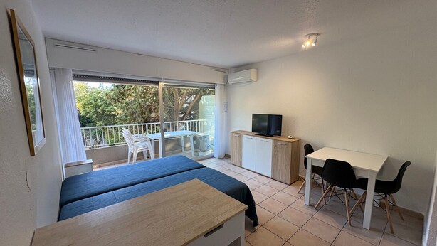 Ein Zimmer mit Bett, Schreibtisch, Fernseher und einem Balkon mit Stühlen.