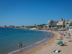 A beach with clear blue water, people sunbathing, and buildings in the background.