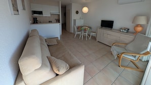 Ein Wohnzimmer mit einer Couch, einem Fernseher, einer Lampe und einem Essbereich mit Stühlen und einem Tisch.