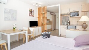 A modern hotel room with a bed, a desk, a TV, a kitchenette, and a bathroom. - Exceptional Location - Air-Conditioned Studio for 2-3 People Near Beach & Shops (Saint-Raphaël)