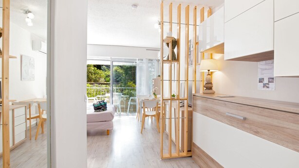 A modern kitchen with wooden cabinets, a dining area with chairs, and a view of the outdoors. - Exceptional Location - Air-Conditioned Studio for 2-3 People Near Beach & Shops (Saint-Raphaël)