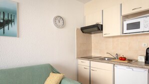 A compact kitchen with a microwave, sink, and a clock on the wall.
