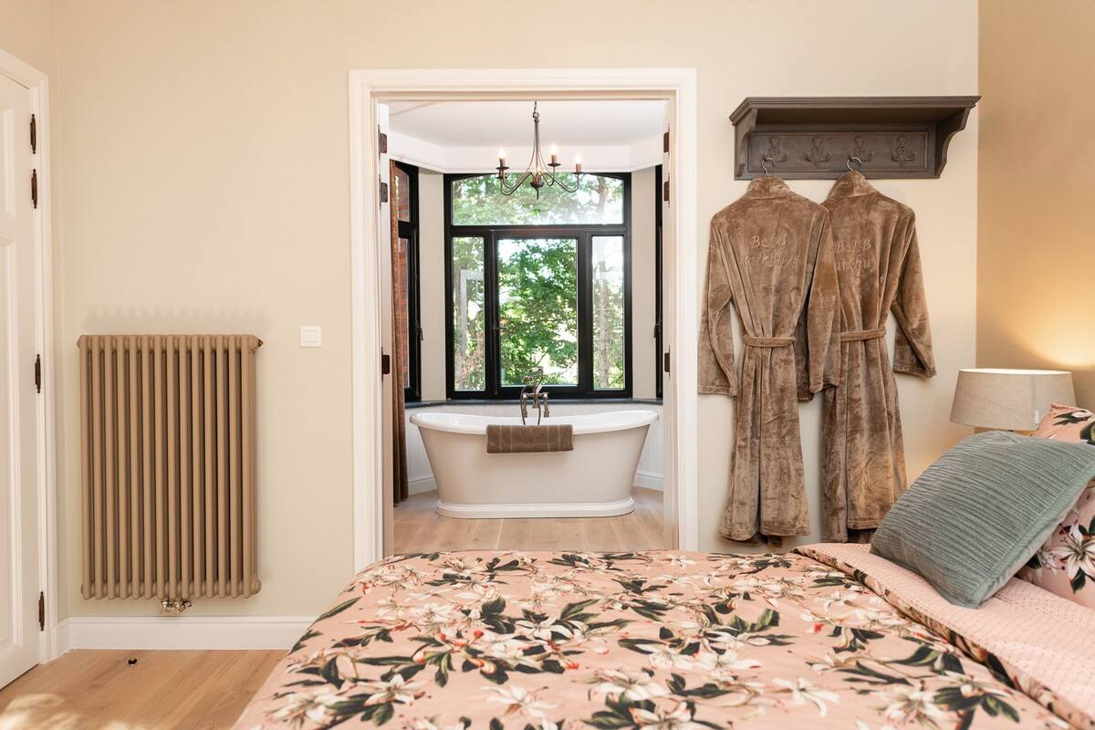 A bedroom with a large bed, a bathtub, and two robes hanging on the wall.