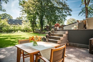 A patio with a wooden table and chairs, a vase of flowers, and a staircase leading to a covered area with potted plants. - B&B Parkhuys (Antwerp)