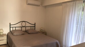 Un lit simple avec une tête de lit, une table de chevet avec une lampe et un appareil de climatisation fixé au mur.