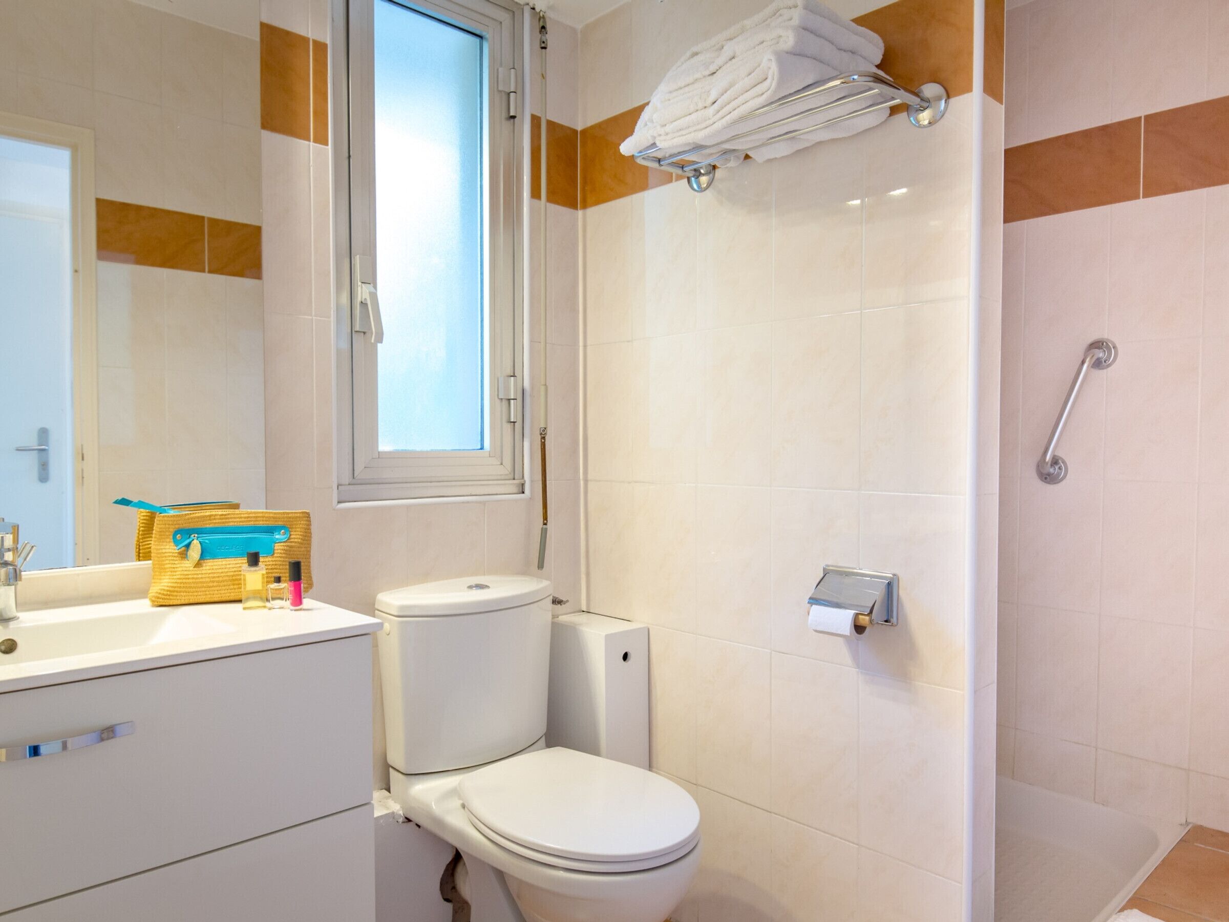 A bathroom with a toilet, a sink, a mirror, a window, and a shower area.