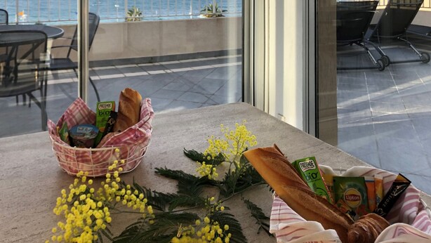 Un balcon offrant une vue sur la mer et les montagnes, avec une table agrémentée de paniers de pain et de fleurs.