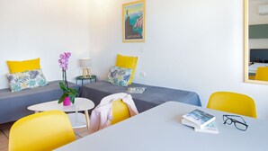 A hotel room with two beds, a small table, a chair, a lamp, and a poster on the wall.