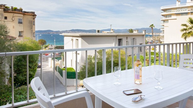A balcony with a white table, two wine glasses, and a bottle of wine.