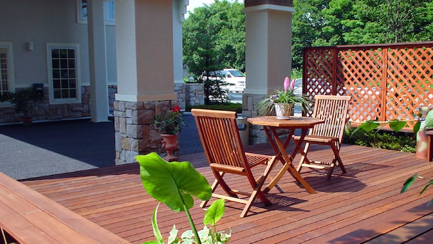 Een houten terras met een tafel en stoelen, omringd door potplanten en een stenen muur.