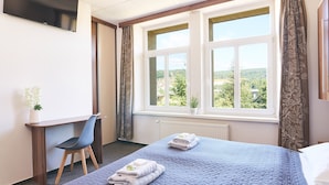 Une chambre d’hôtel équipée d’un lit, d’un bureau, d’une chaise et d’une fenêtre donnant sur un paysage verdoyant.
