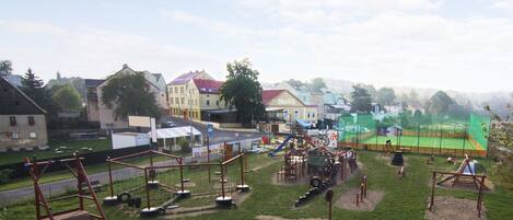 A playground with various play structures, a tennis court, and residential buildings in the background.