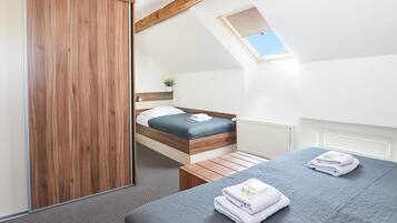 A modern bedroom with a sloped ceiling, a skylight, a wooden wardrobe, a bed with a blue mattress, and a bedside table with towels.
