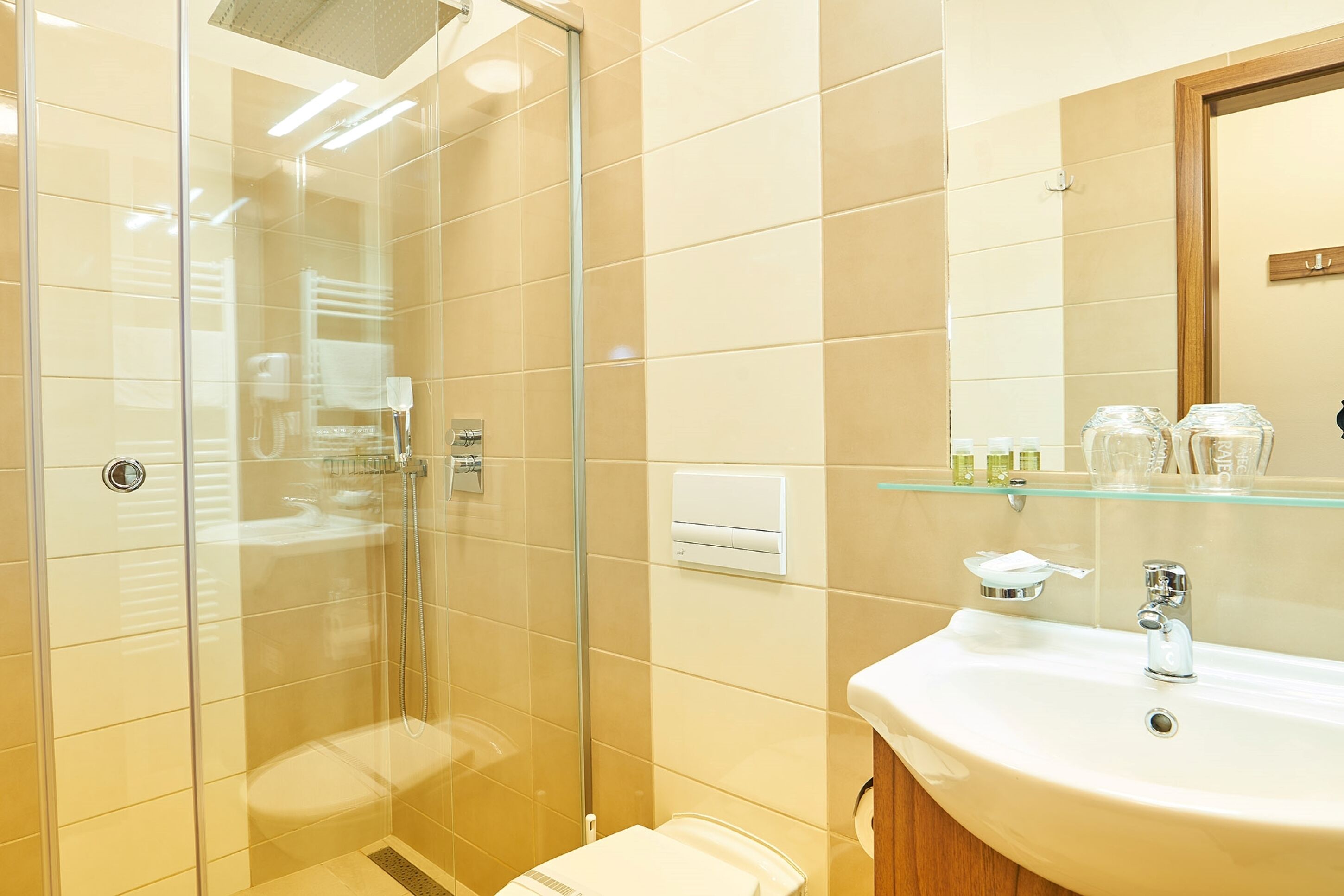A modern bathroom with a glass-enclosed shower, a sink with a mirror, and toiletries on a shelf.