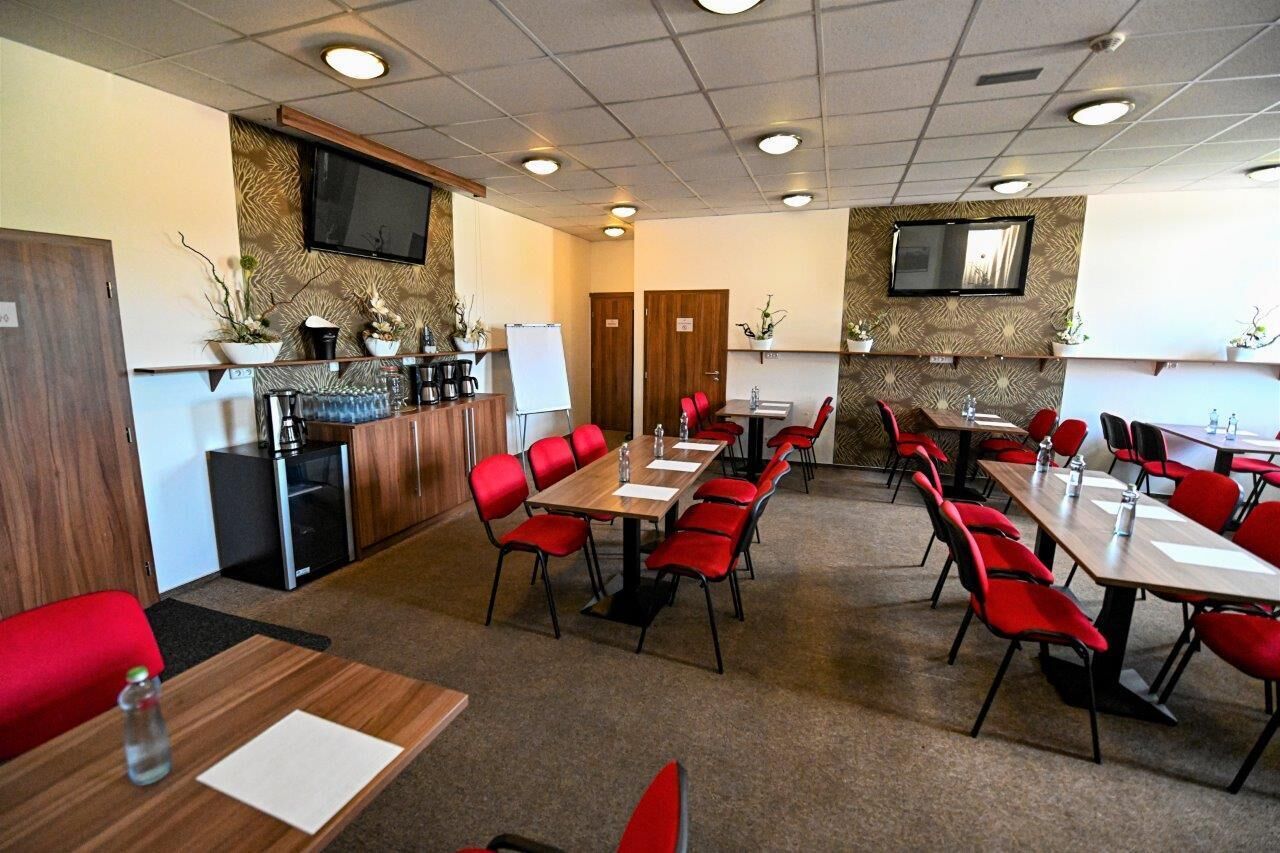 A conference room with multiple tables and red chairs, equipped with water bottles and papers.