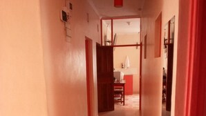 Un couloir étroit avec des carreaux de sol à motifs, une porte rouge sur la droite et, au fond, une pièce visible avec une table et des chaises.