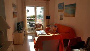 Ein gemütliches Wohnzimmer mit Sofa, Fernseher, Tisch und einem Balkon mit Gartenmöbeln.