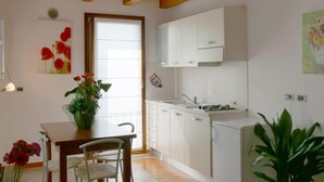 Une cuisine avec des meubles blancs, une table en bois et des chaises. Il y a une fenêtre donnant sur l’extérieur.