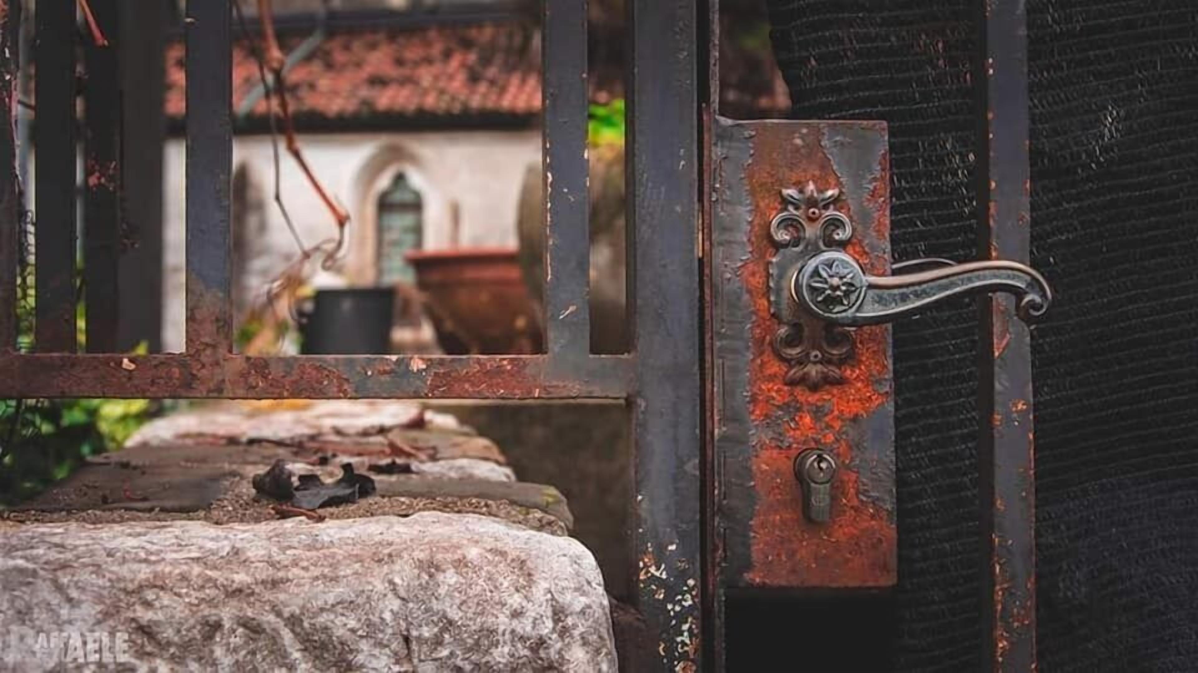 A metal gate with a decorative handle and a keyhole, leading to a stone pathway.