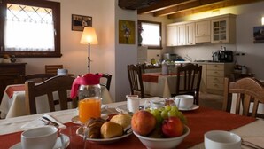 Une table de petit-déjeuner dressée avec des croissants, des fruits et du jus d’orange, donnant sur une cuisine et un coin repas.