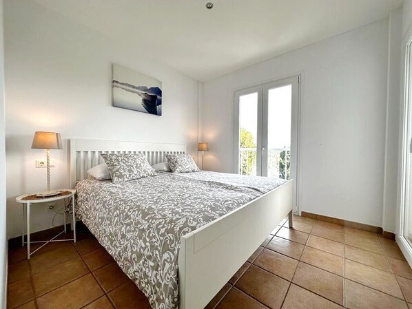 A bedroom with a bed, two bedside tables, a window, and a painting on the wall.