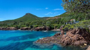 Un paysage côtier caractérisé par une eau turquoise cristalline, des rivages rocheux et une colline en arrière-plan.