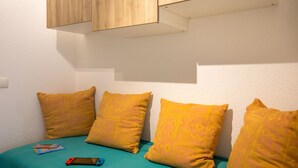 Une chambre avec un lit, trois oreillers jaunes, une couvre-lit turquoise et une armoire en bois placée au-dessus du lit.