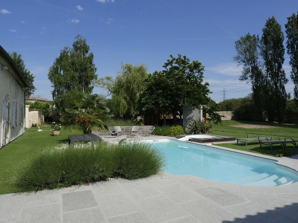 A swimming pool with a stone deck, surrounded by a well-maintained lawn and trees.