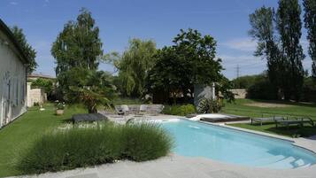 A swimming pool with a stone deck, surrounded by a well-maintained lawn and trees.