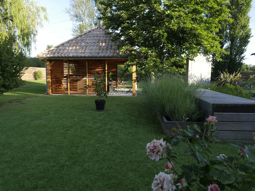 Een houten prieel met pannendak in een verzorgde tuin.