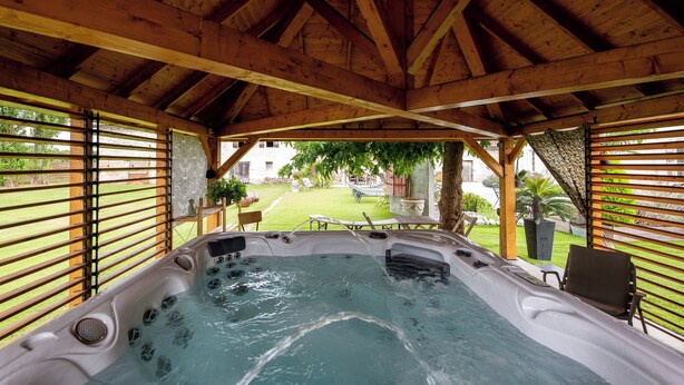 A hot tub under a wooden roof with a view of a grassy yard and a patio area. - Le Domaine d'Ardgalen (Val de Virvée)