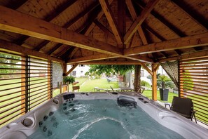 Un bain à remous sous une toiture en bois, avec vue sur une pelouse et un espace patio.