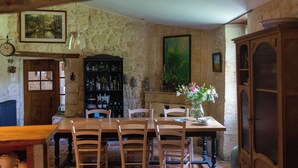 A rustic dining room with a wooden table and chairs, a bookshelf, and a large painting on the wall. - Le Domaine d'Ardgalen (Val de Virvée)