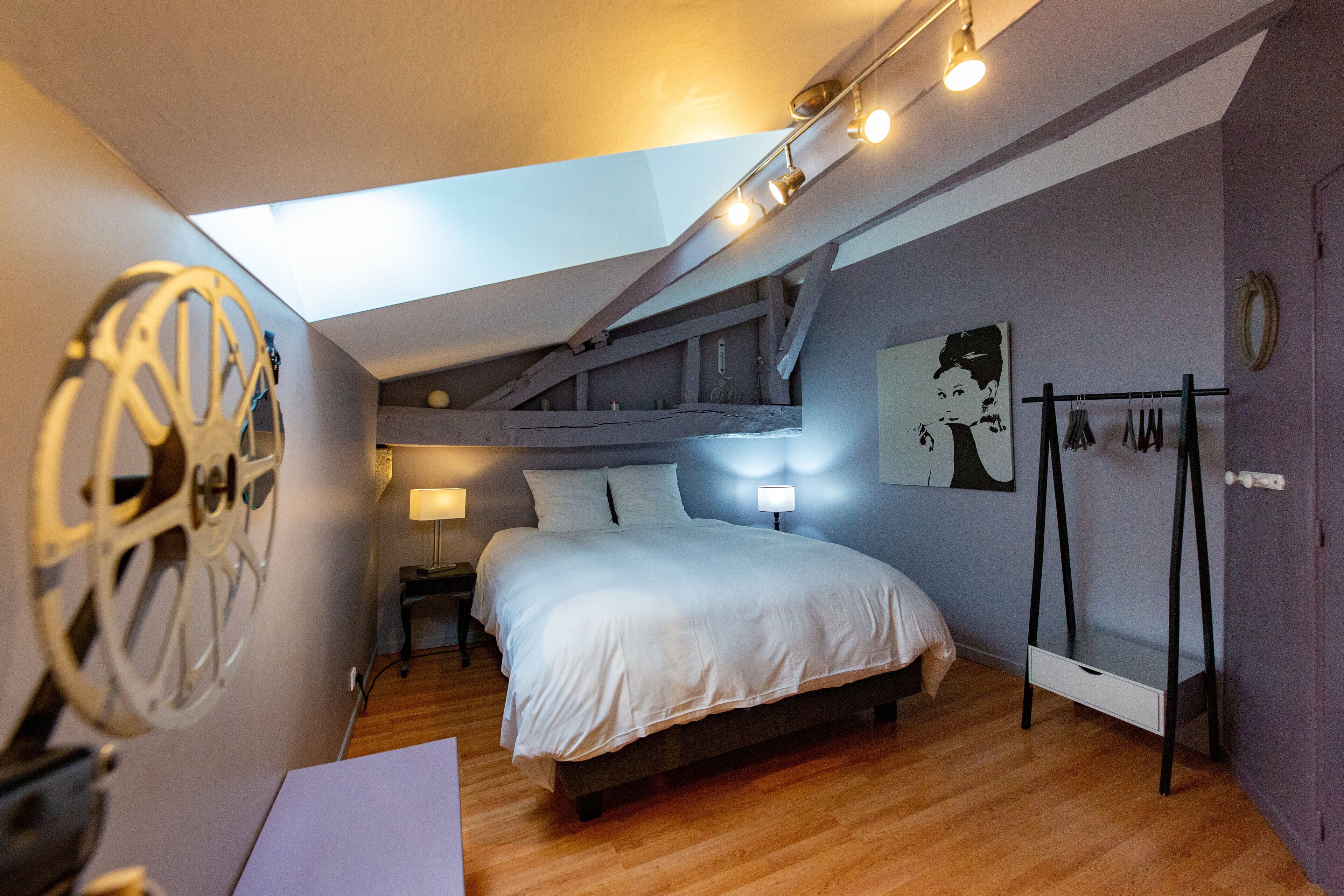 A bedroom with a bed, a desk, a lamp, a coat rack, and a wall with a circular decoration.