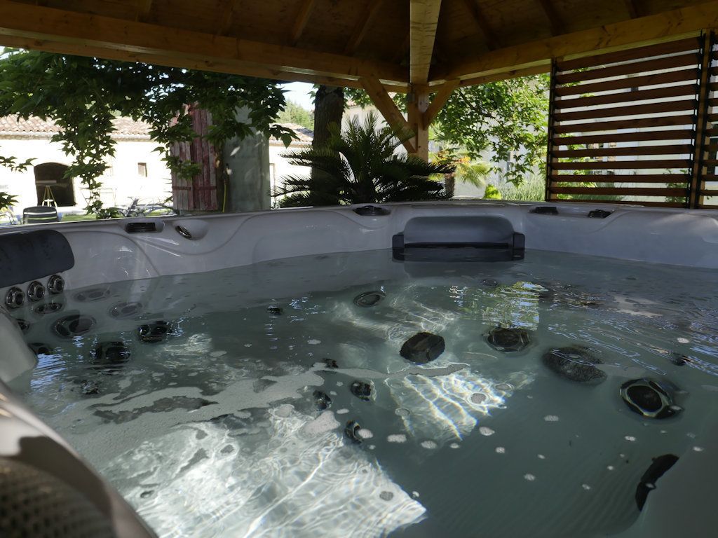 A hot tub with multiple jets, surrounded by a wooden pergola and plants.