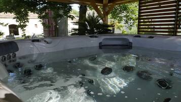 Un jacuzzi con múltiples chorros, rodeado por una pérgola de madera y plantas.