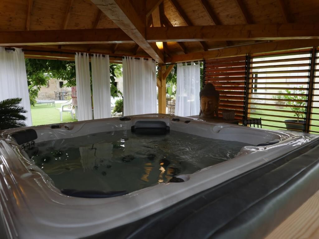 Un bain à remous situé dans un espace extérieur abrité, agrémenté de poutres en bois et de rideaux blancs.