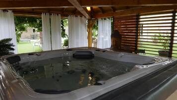 Un bain à remous situé dans un espace extérieur abrité, agrémenté de poutres en bois et de rideaux blancs.