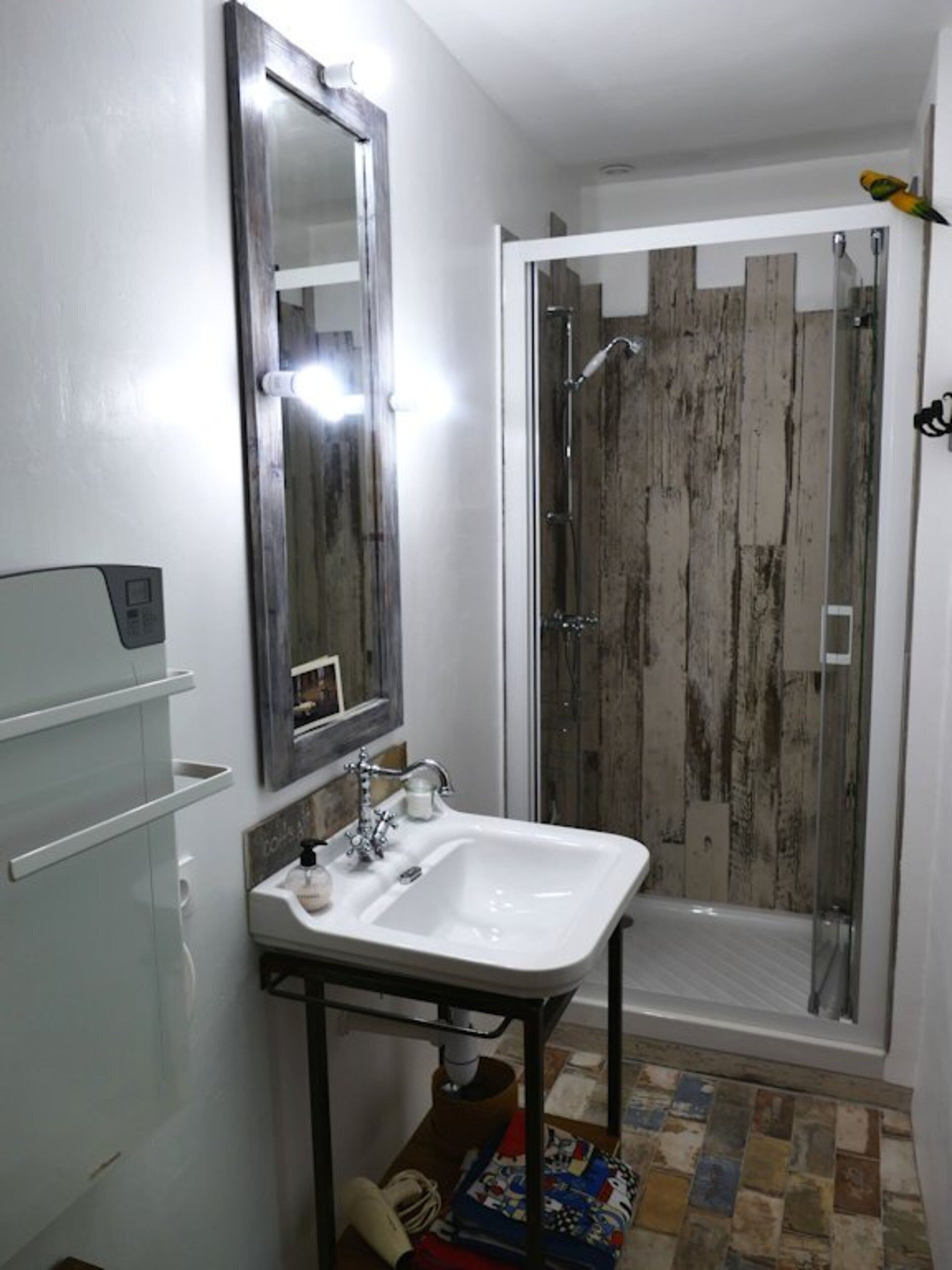 Un baño con lavamanos blanco, un espejo y una ducha con pared de madera.