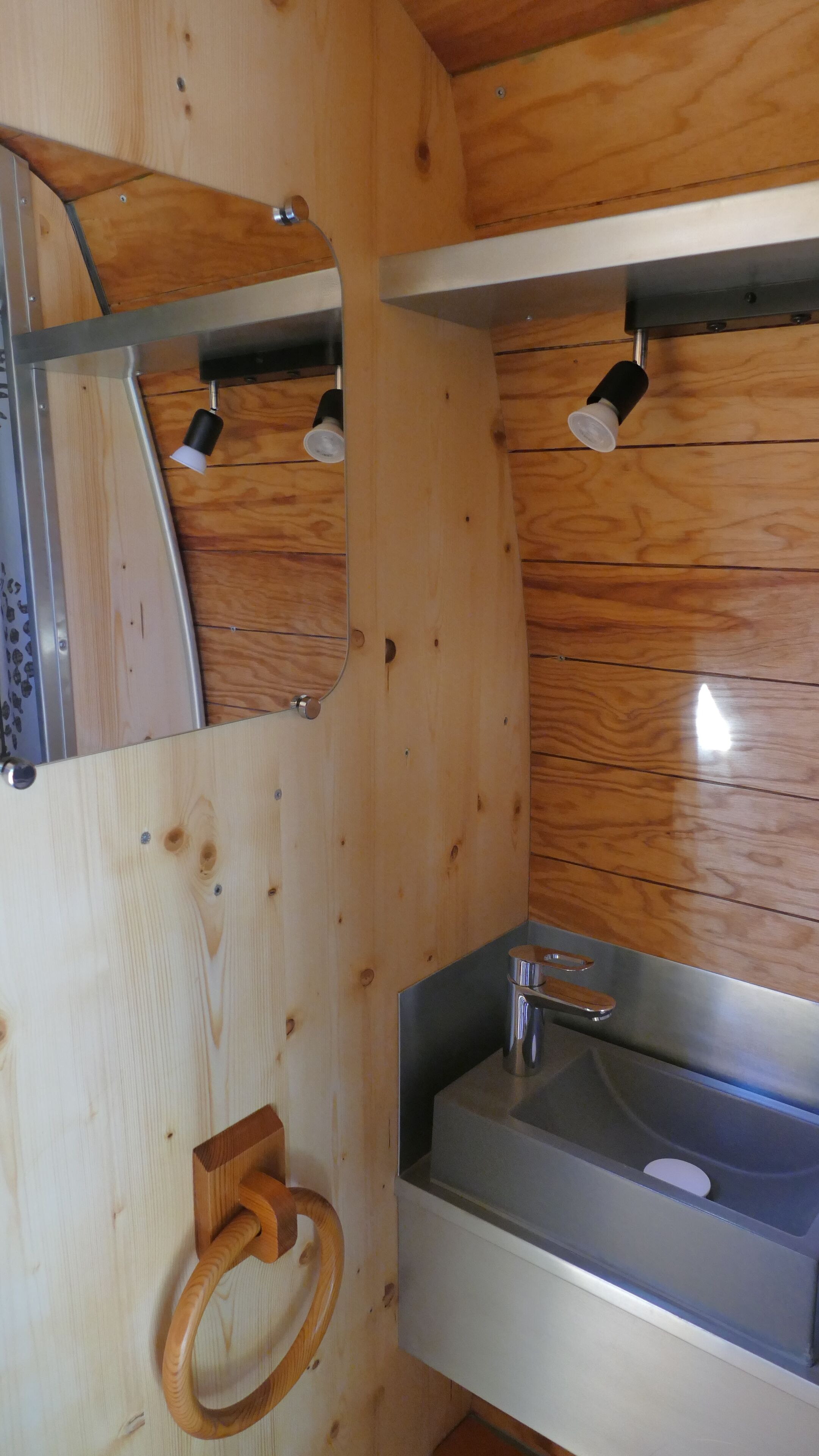 A wooden cabin interior with a metal sink, a mirror, and a wooden towel ring.