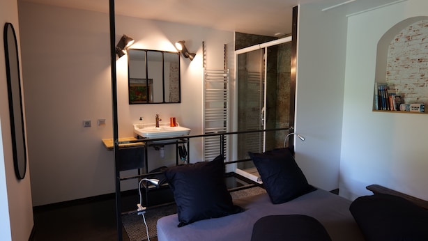 Une chambre moderne avec un grand lit, une table de chevet, un miroir, un lavabo intégré et un espace douche.