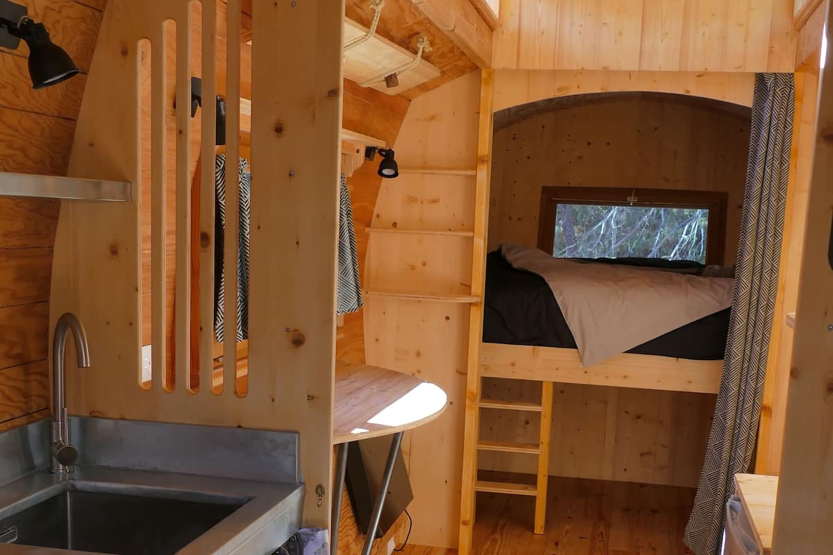 Une petite cabane en bois comprenant un lit superposé, un coin cuisine et une fenêtre donnant sur l’extérieur.
