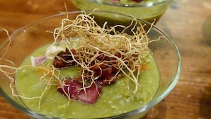 Un bol de soupe verte garni de lardons croustillants et de fines lamelles d’une préparation croustillante.