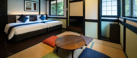 A hotel room with a bed, a small table, and a window with a view of greenery.