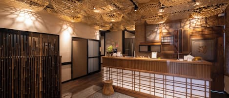 A traditional Japanese interior with a reception desk, bamboo partitions, and a ceiling with woven paper lampshades.