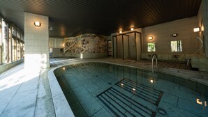 Piscina com chão ladrilhado, ralo e parede com mural. Há luzes no teto e nas paredes, e uma janela no lado esquerdo.