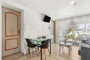 A dining area with a table and chairs, a television mounted on the wall, and a view through a glass door.