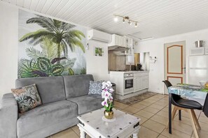 A living room with a gray sofa, a coffee table with a vase, and a kitchen area with white cabinets and a microwave.