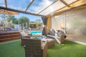 An outdoor patio with wicker furniture, a pool, and a covered area with a view of the surrounding landscape.